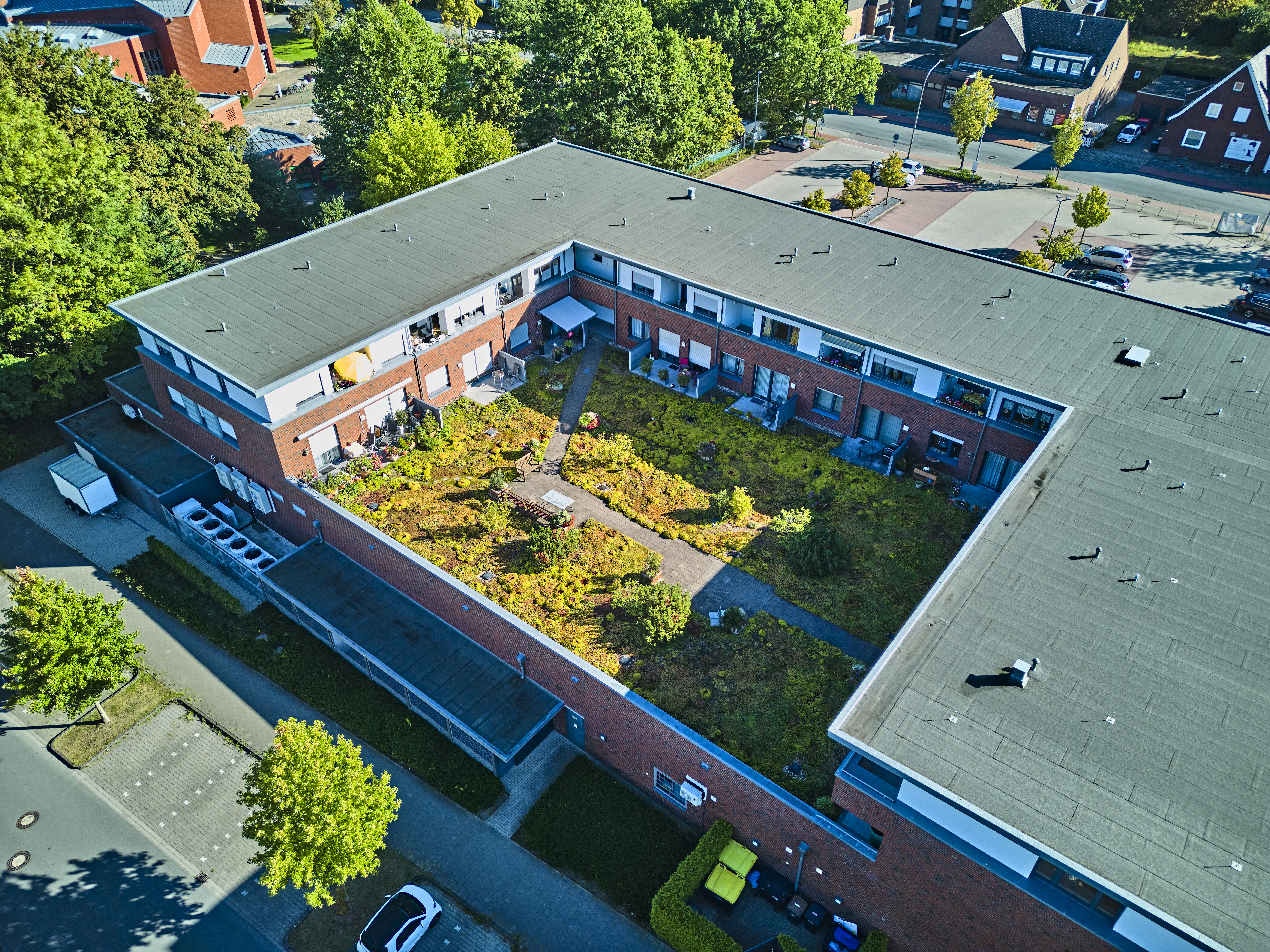`alt="Luftbild eines U-förmigen Klinker-Mehrfamilienhauses mit extensiv begrüntem Innenhof auf dem Flachdach."`